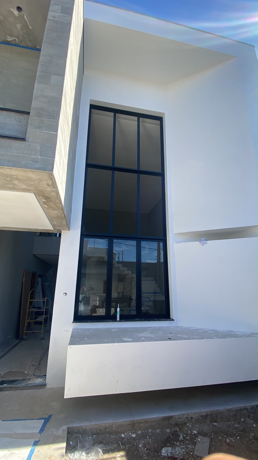 Fachada branca com janela alta de vidro refletivo em esquadria preta